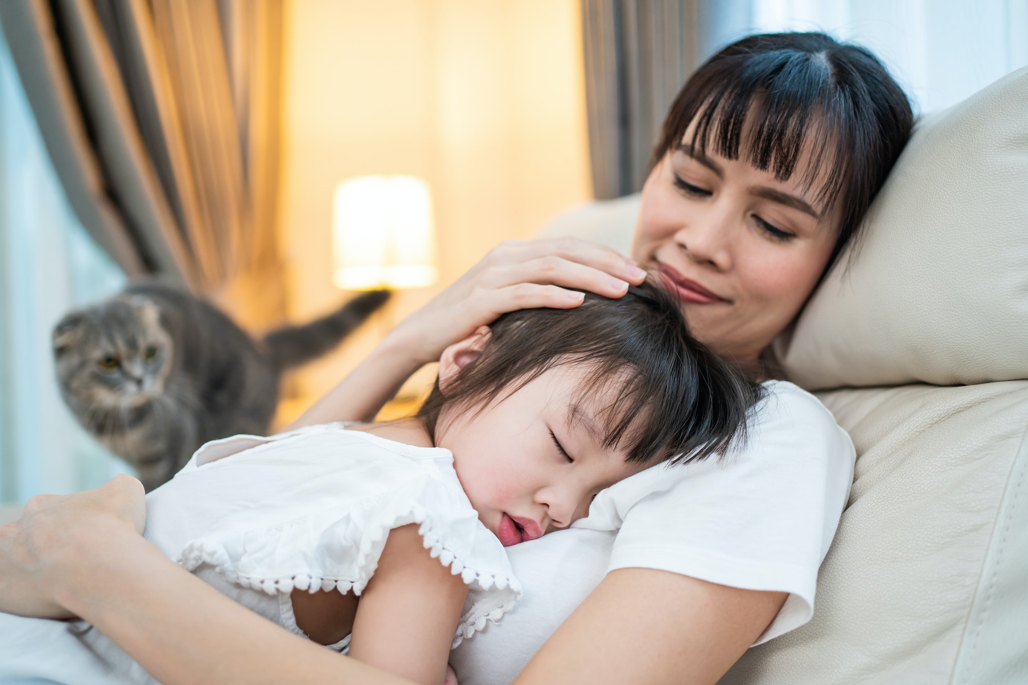 asian-beautiful-loving-mother-hugging-sleeping-baby-girl-in-her-arms-on-sofa-at-home